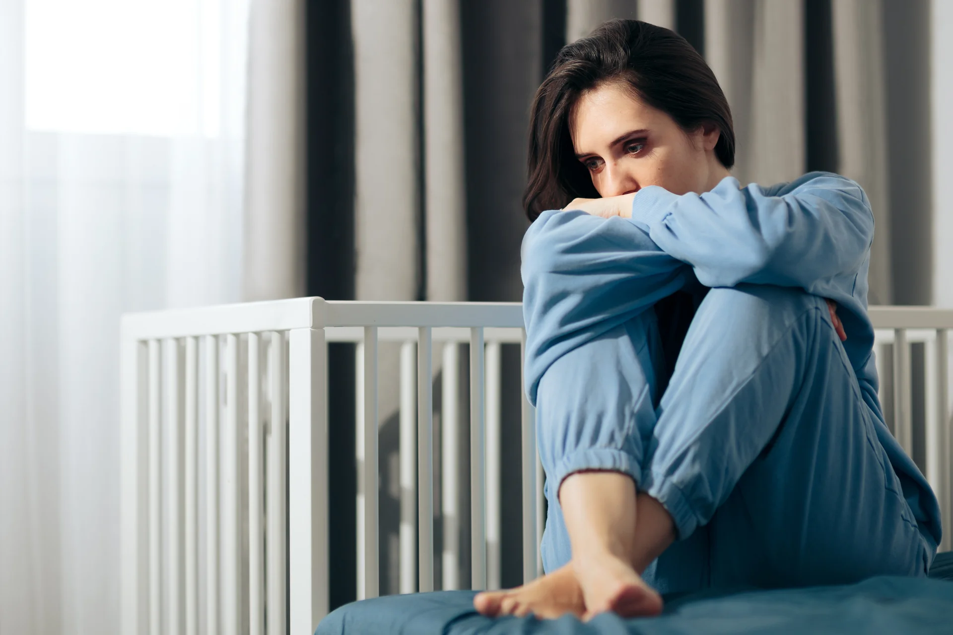 Femme pensive regardant par la fenêtre, symbolisant le processus de deuil périnatal