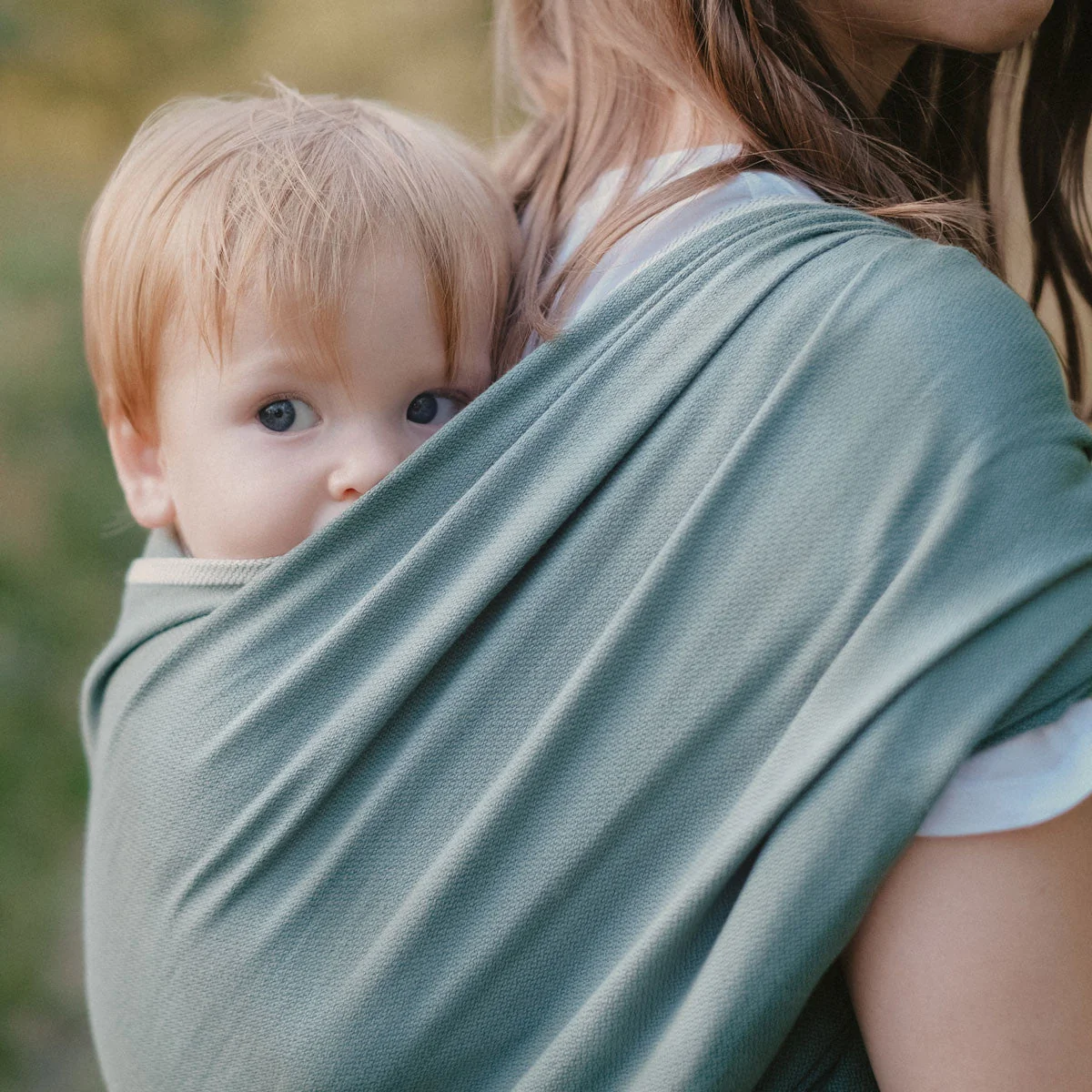 Maman portant son bébé dans une écharpe de portage tissée vert eucalyptus