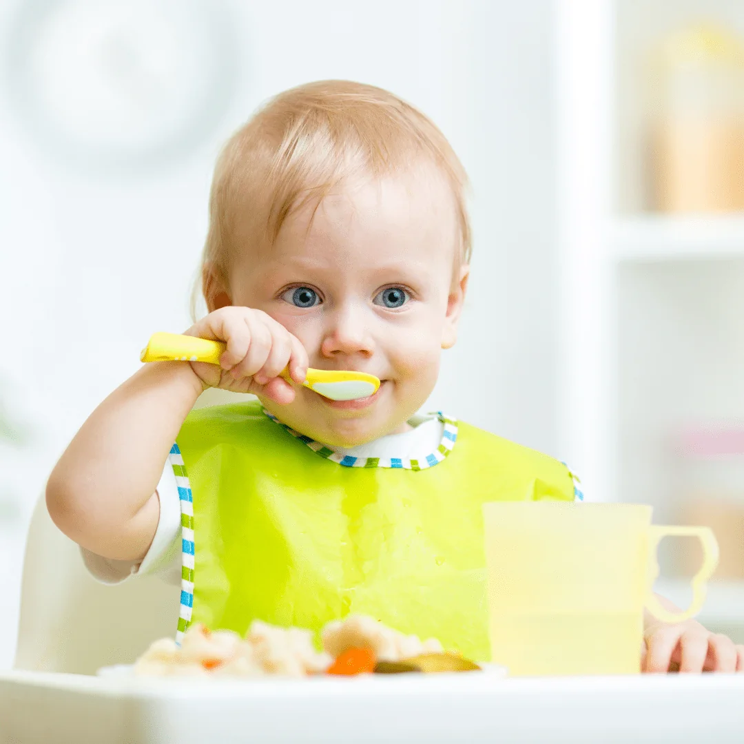 Jeune enfant apprenant à manger seul dans sa chaise haute à table