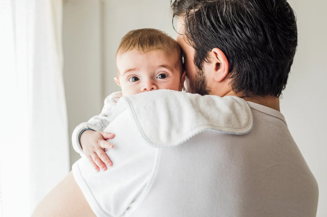 Papa tenant son bébé sur l'épaule pour l'aider à faire son rot après la tétée.