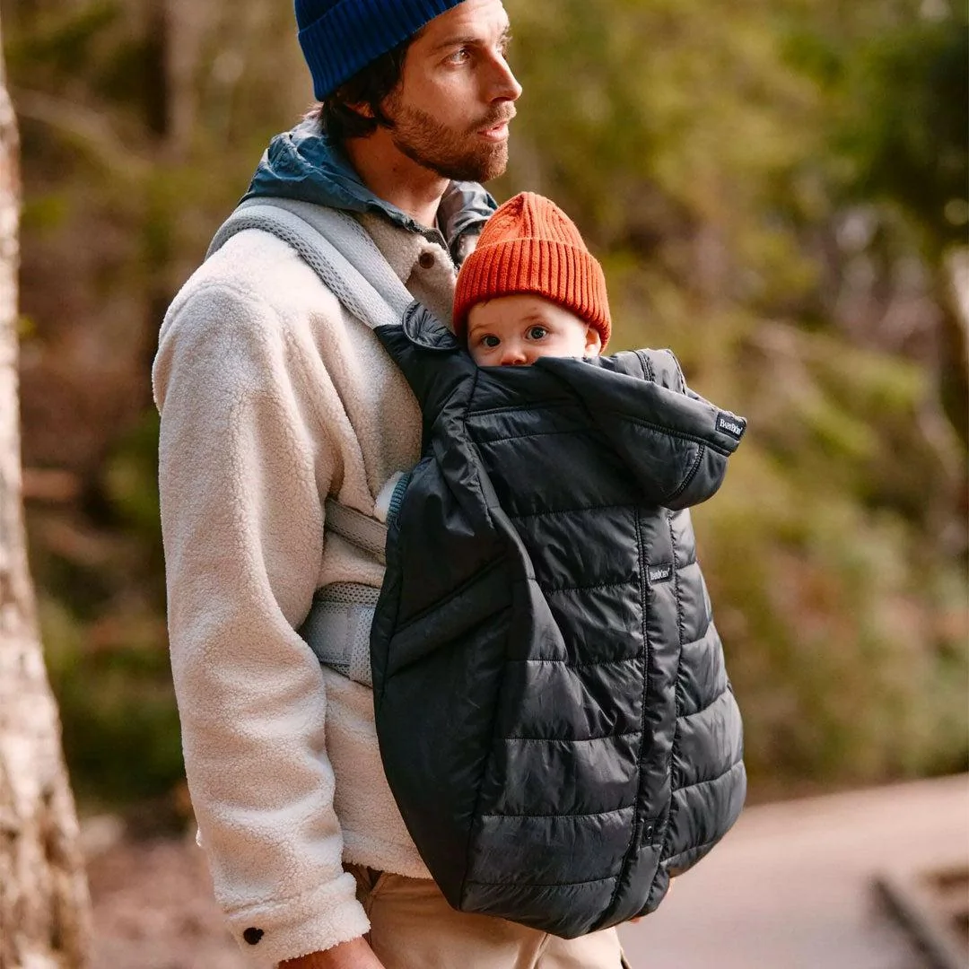 Parent utilisant une couverture de portage pour protéger bébé du froid en hiver.