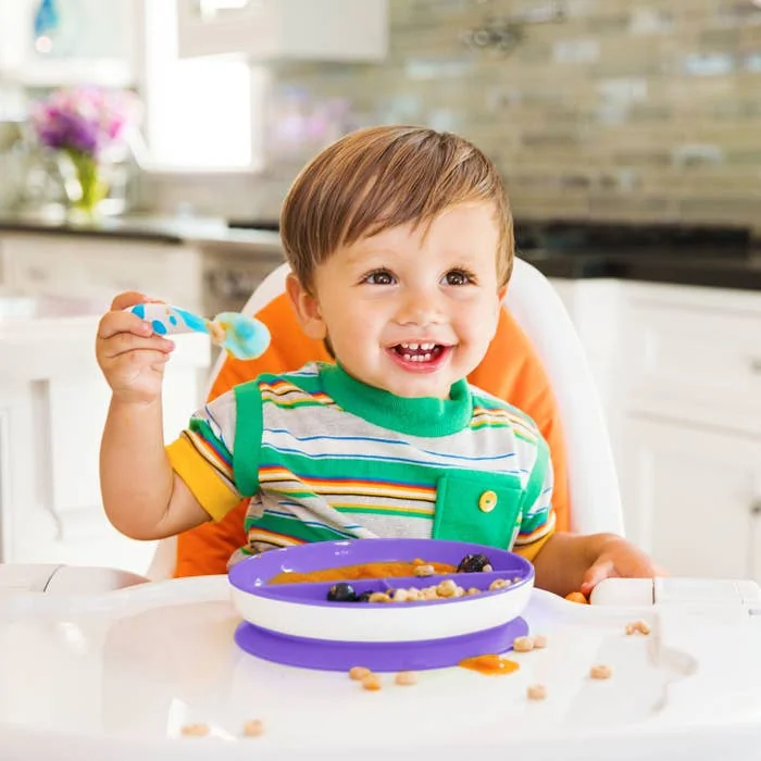 Enfant souriant dans sa chaise haute avec une assiette à ventouse, rendant le repas plus serein