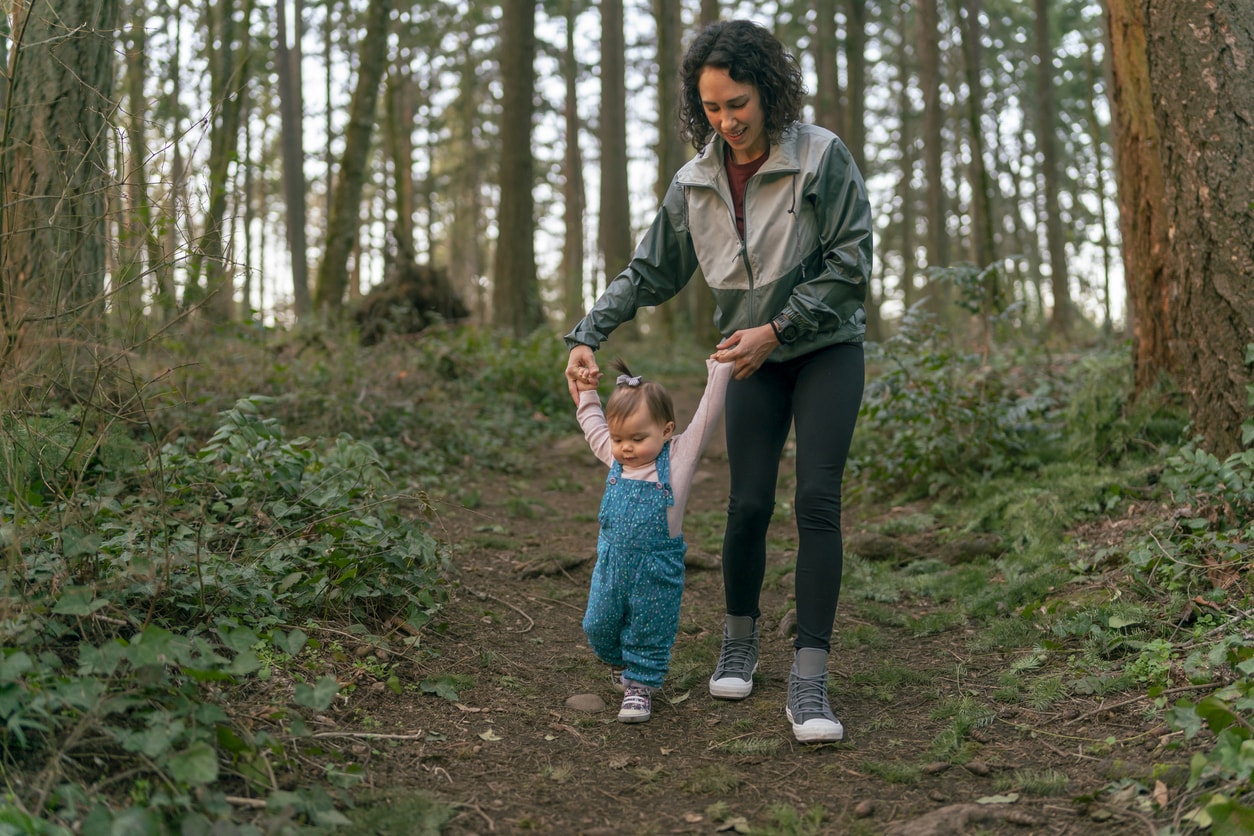 Maman aidant bébé à marcher dans la forêt au coucher du soleil