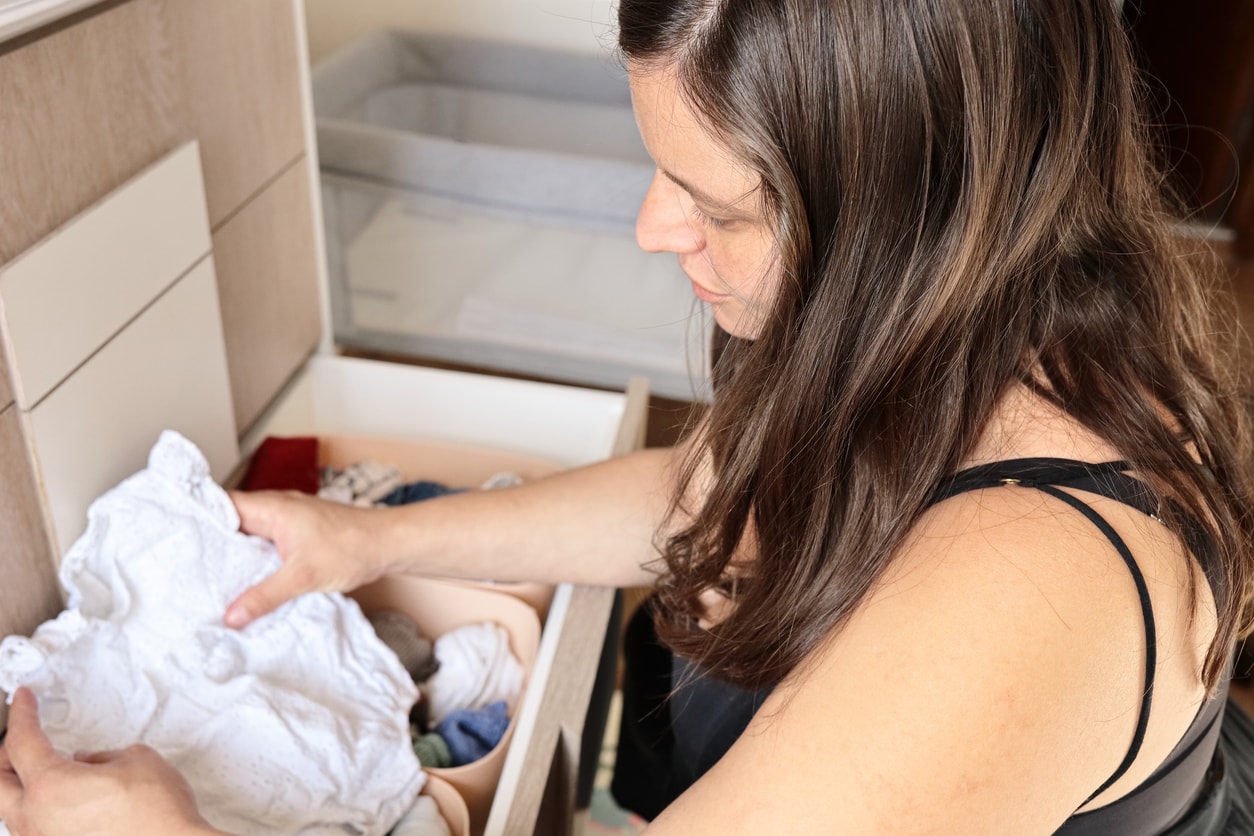 Une jeune maman triant avec émotion les vêtements de son bébé dans une chambre douce