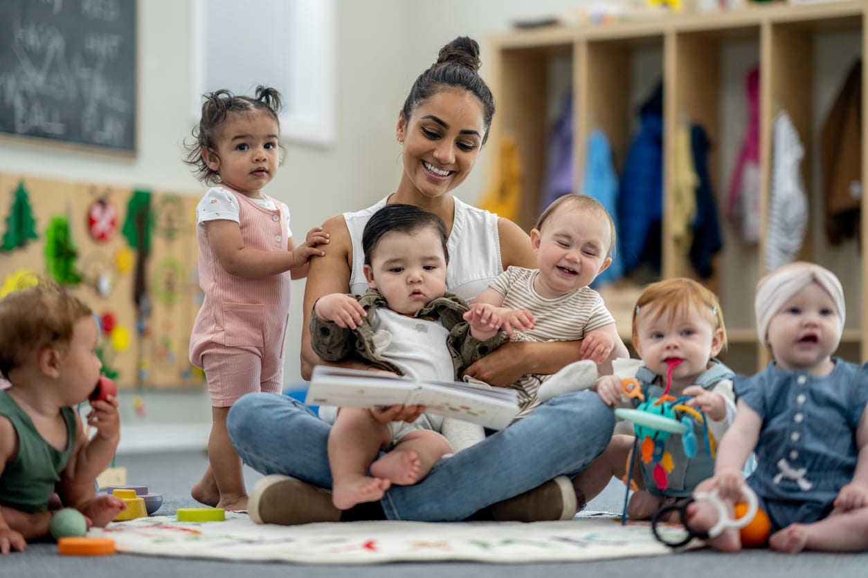 Une professionnelle de la petite enfance assise avec un groupe de bébés, leur lisant un livre dans leur salle.