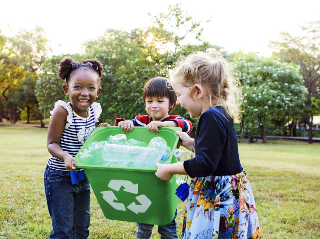 Enfants souriants derrière un bac de recyclage vert