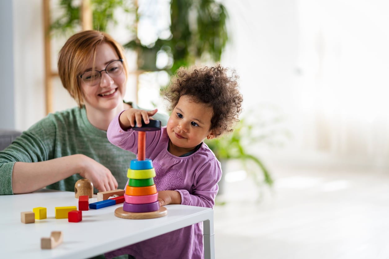 Une professionnelle regardant un enfant jouer avec un jouet éducatif.
