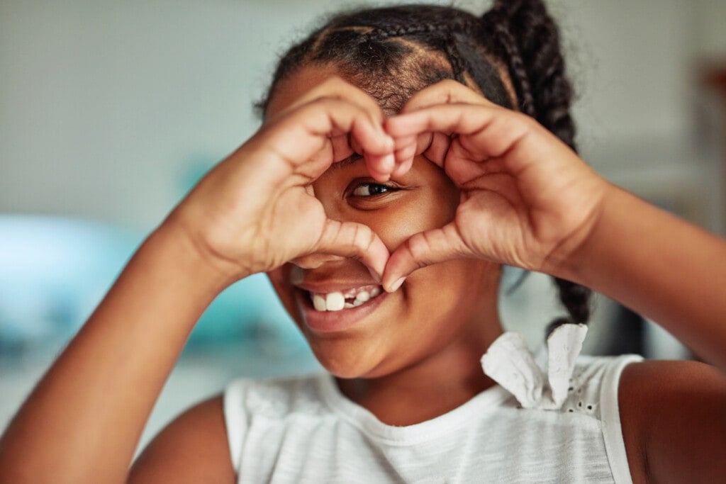 Une petite fille souriante formant un cœur avec ses mains sur son visage