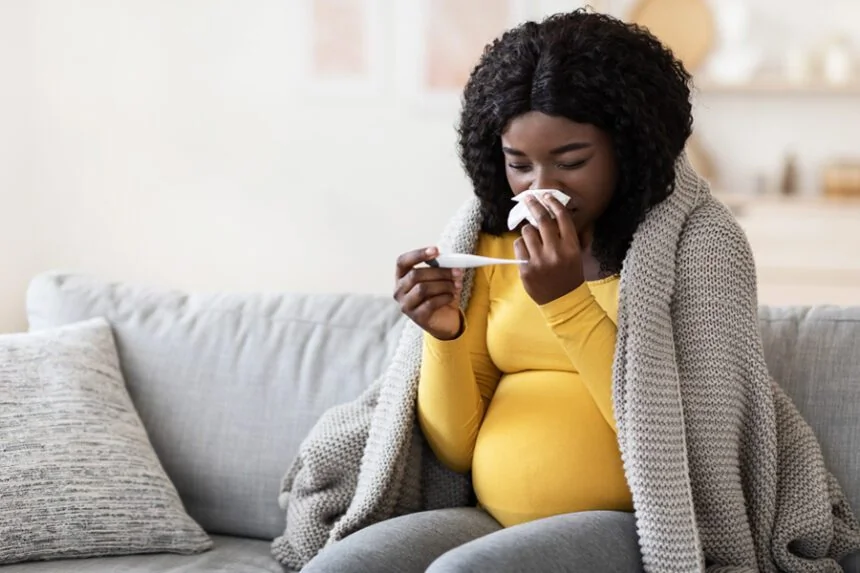 Femme enceinte malade au lit avec un thermomètre et des mouchoirs.