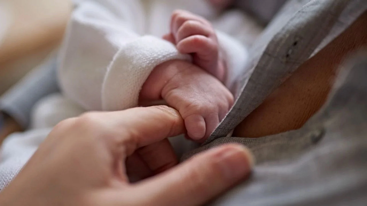 Main fragile d'un bébé prématuré tenant le doigt d'un parent pour montrer sa petite taille.